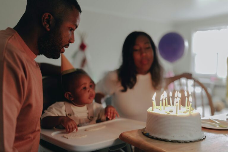 A parent and baby celebrate a first birthday at home, gathered around a cake with lit candles, symbolizing major life milestones that often prompt updates to estate planning and wills.