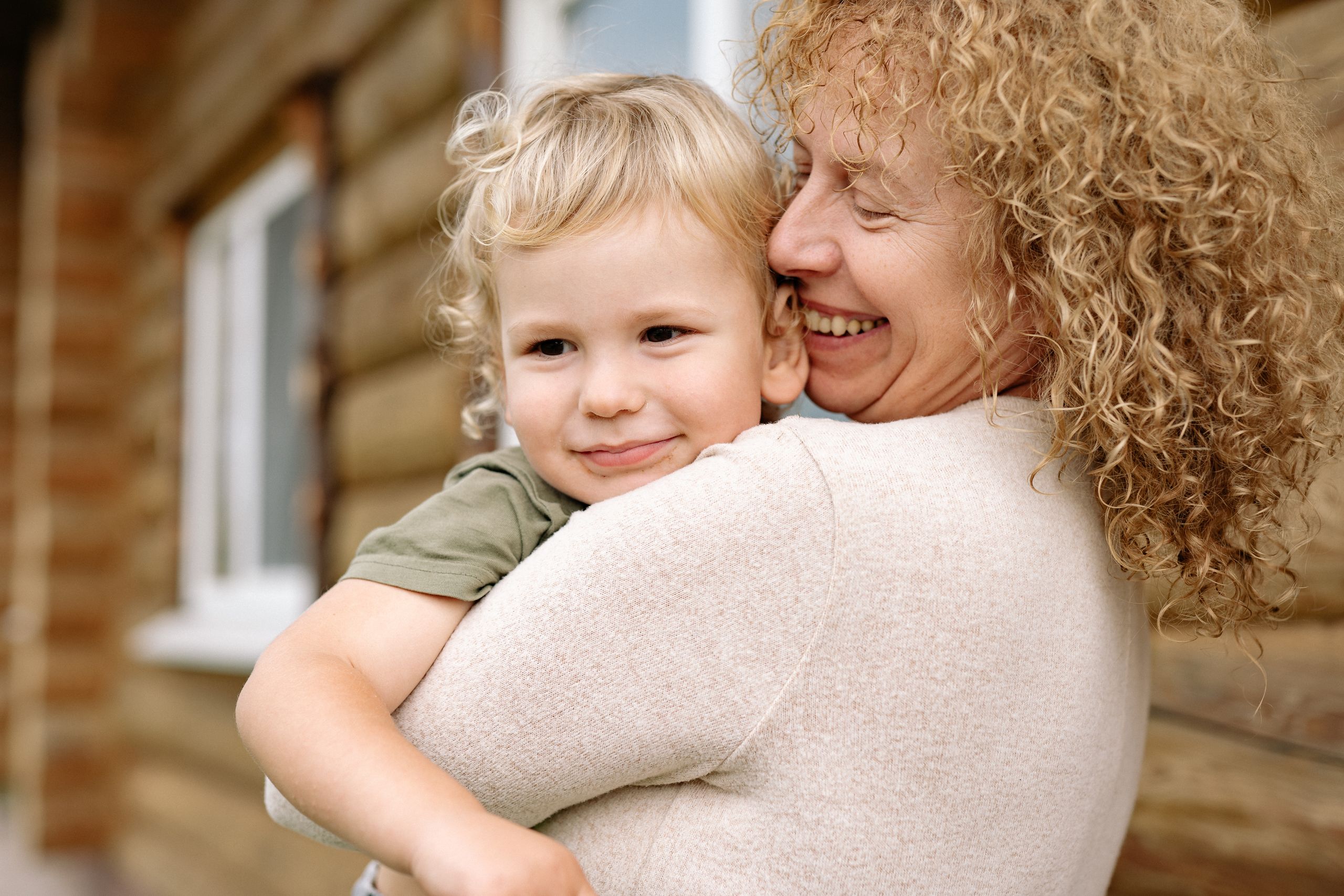 A smiling grandmother hugging her happy young grandson outside their home
